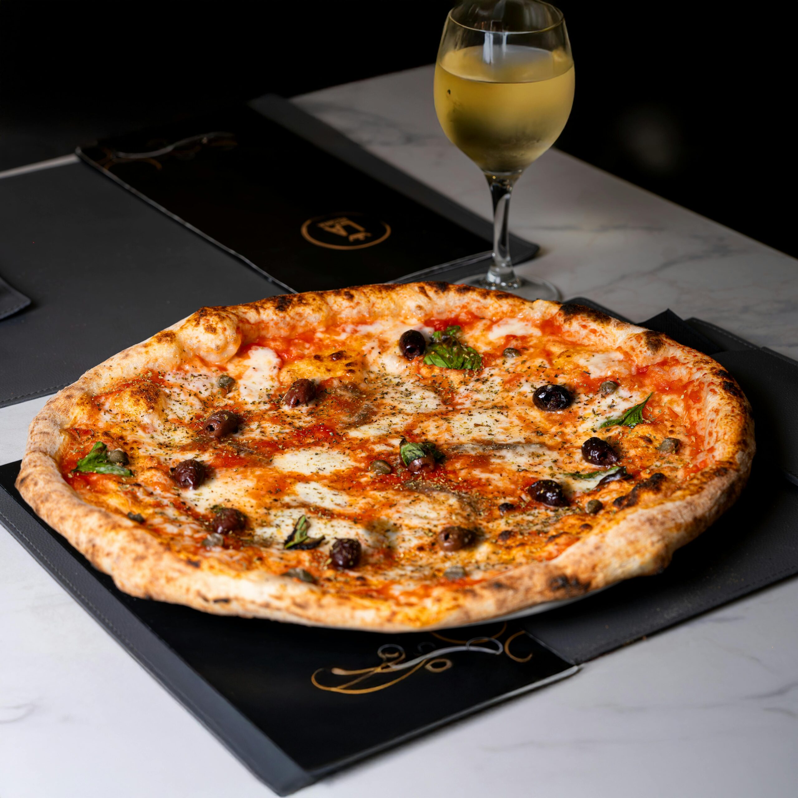 Tasty Neapolitan pizza paired with white wine on elegant table setting.